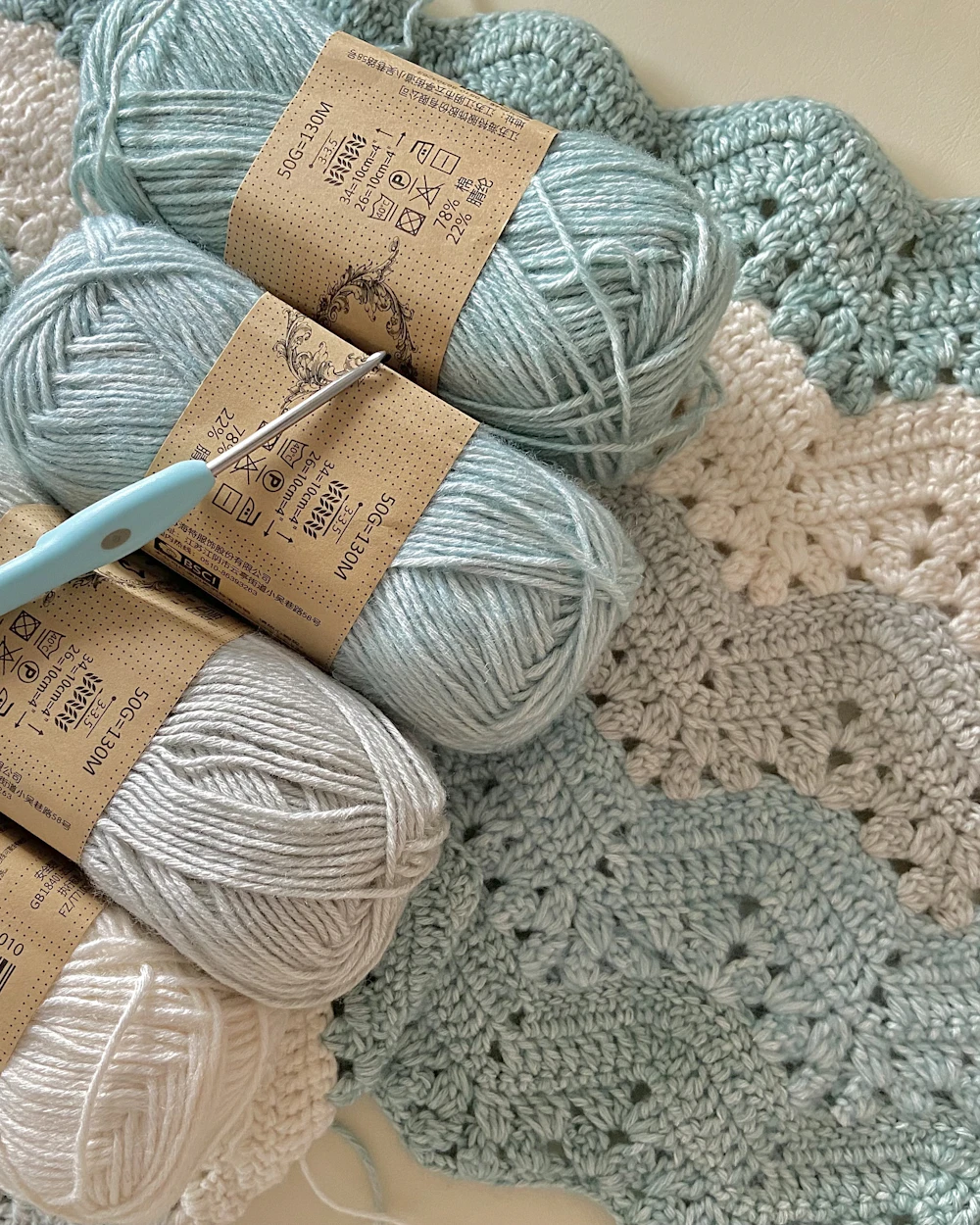 Sage yarn balls with a crochet hook on a granny square