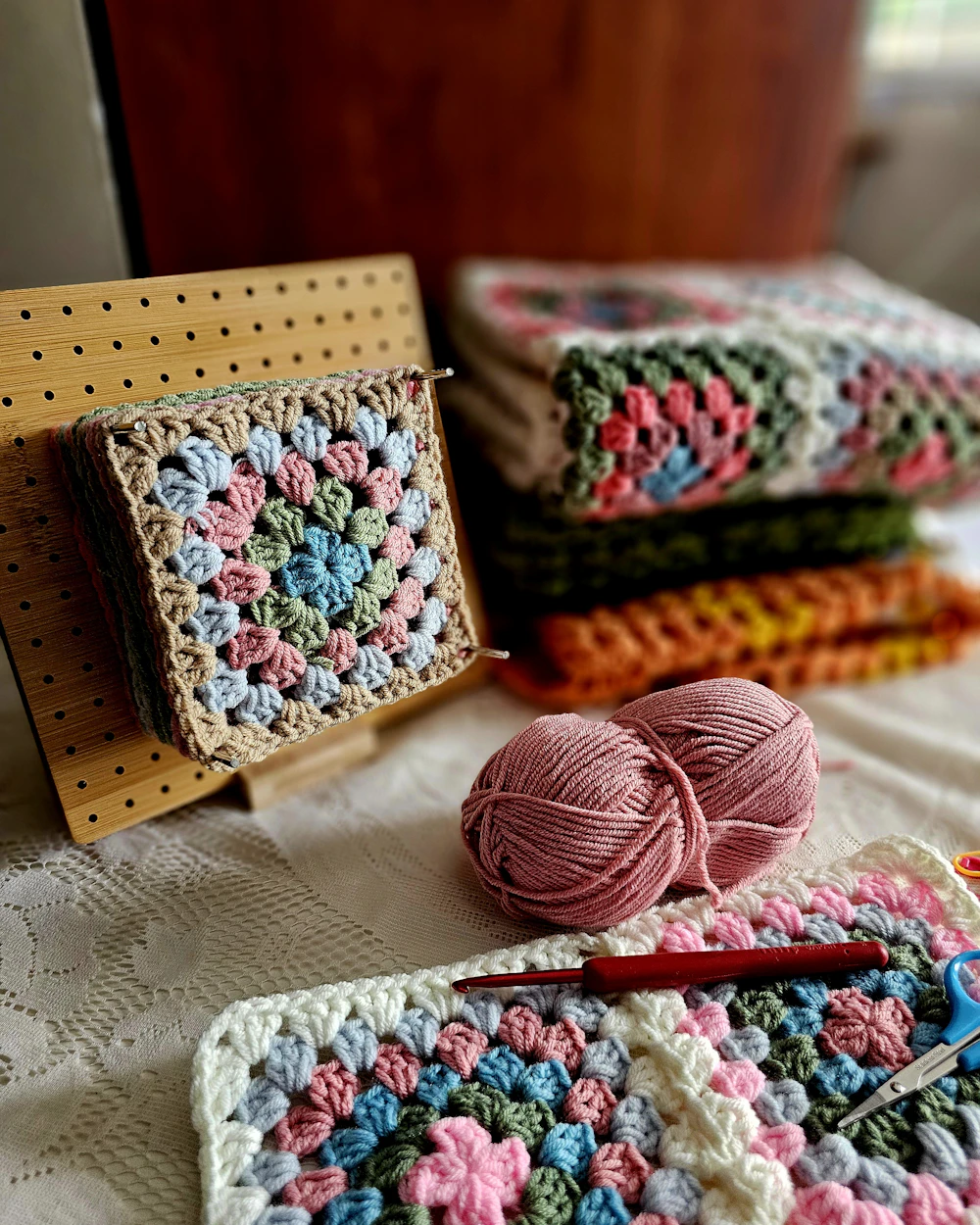 Pink yarn ball beside a stack of floral granny squares